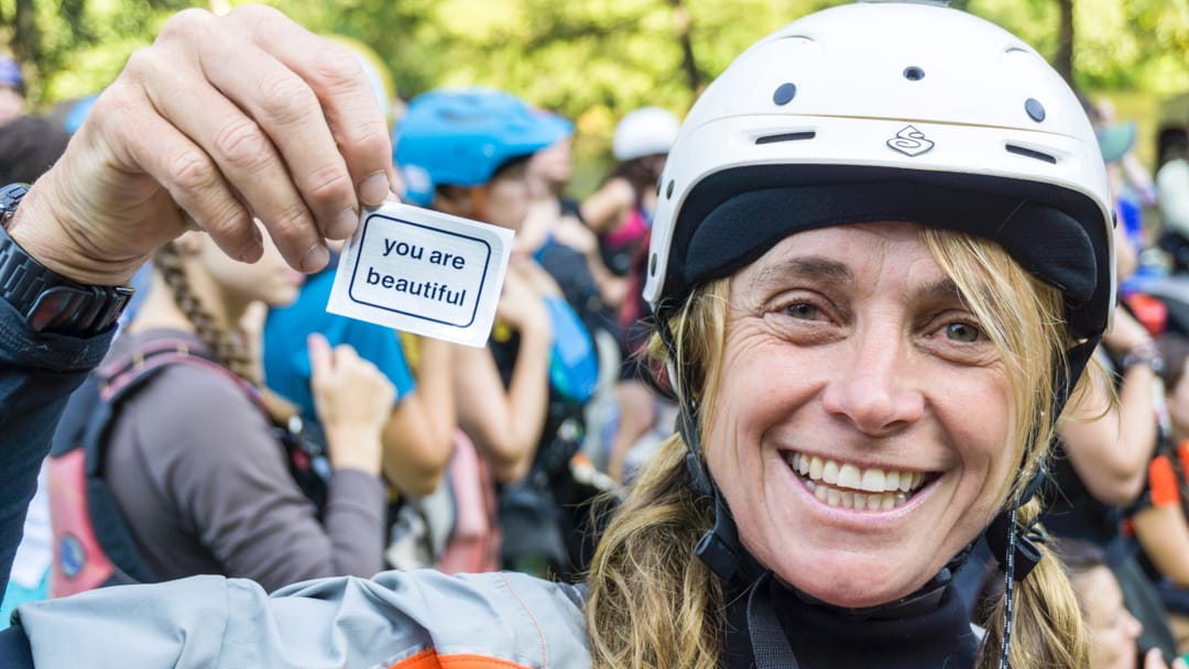 Woman in paddling gear holding a "you are beautiful" sticker