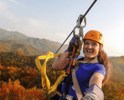 a woman zip lines across a background of fall colored mountains