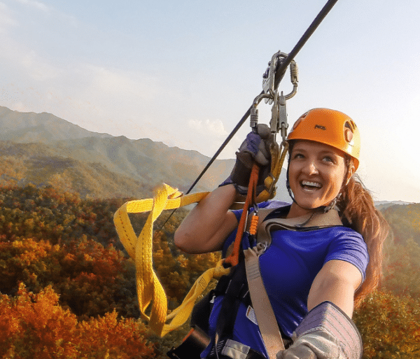 a woman zip lines across a background of fall colored mountains