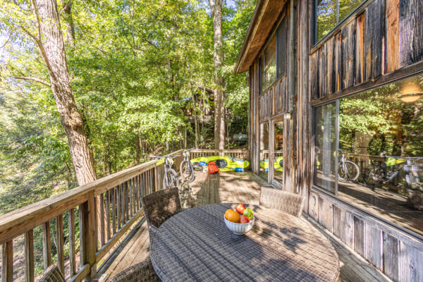 cabin deck with wooden railing, fruit bowl with oranges and apples, and kayak laying on side