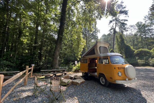 a yellow VW van is parked in a camping spot with fire pit.