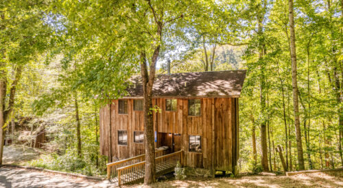 front outside of cabin with windows, green tree leaves and railing