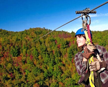 women zip lining in mid air with the green, orange, and red trees on the horizon