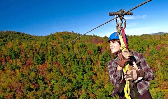 women zip lining in mid air with the green, orange, and red trees on the horizon