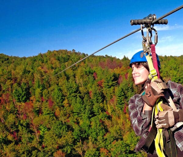women zip lining in mid air with the green, orange, and red trees on the horizon