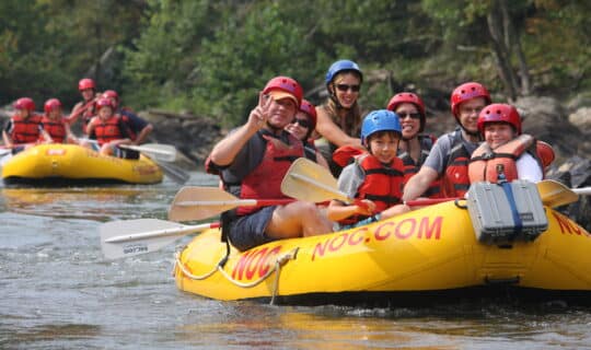 kids and a dad float down the river in a yellow raft while enjoying a day of french broad river rafting.
