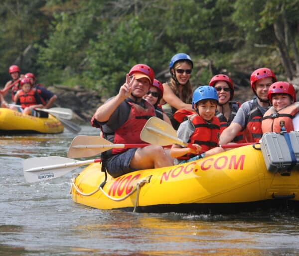 kids and a dad float down the river in a yellow raft while enjoying a day of french broad river rafting.