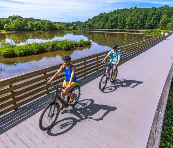 Two adults biking by water on the Chattahoochee River Bike Rentals – Roswell trip