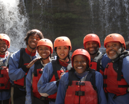 a group of people dressed in red and blue river gear stand in front of a waterfall at the chattooga river.