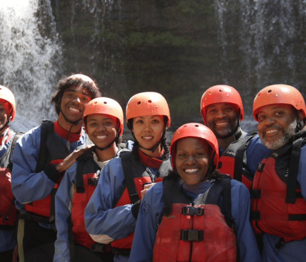 a group of people dressed in red and blue river gear stand in front of a waterfall at the chattooga river.