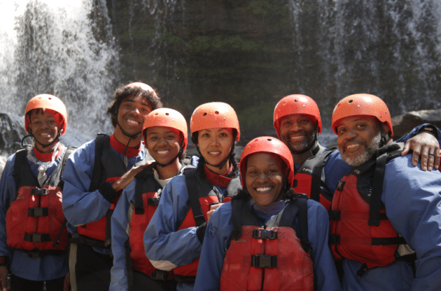 a group of people dressed in red and blue river gear stand in front of a waterfall at the chattooga river.