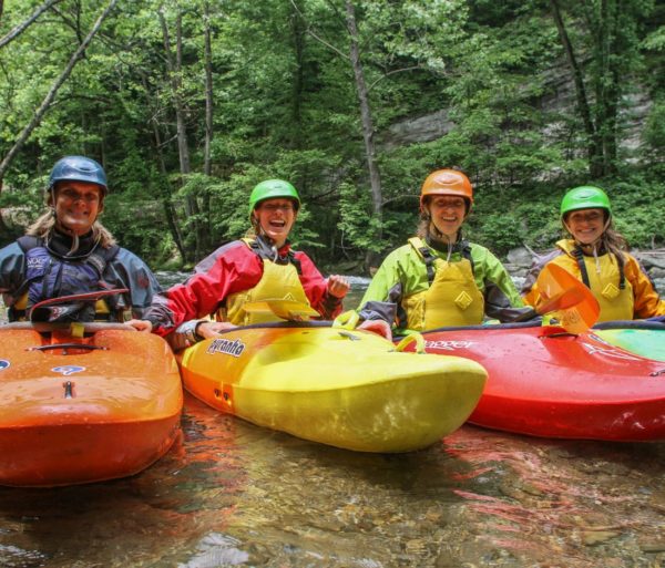 Four women in kayaks smiling during the Introduction to Whitewater Kayaking Course