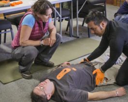 Student practicing medical techniques on man laying down during the Wilderness First Aid (WFA) Certification Course