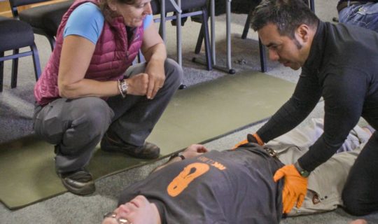 Student practicing medical techniques on man laying down during the Wilderness First Aid (WFA) Certification Course