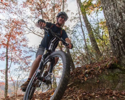 Close up of mountain biker riding through forest in autumn.