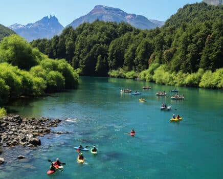 kakayers and rafters paddle the blue waters of the futaleufu river amongst towering green mountains