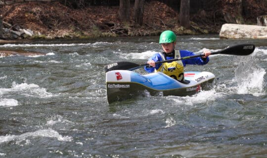 a young girl in a kayak races down in splashy water