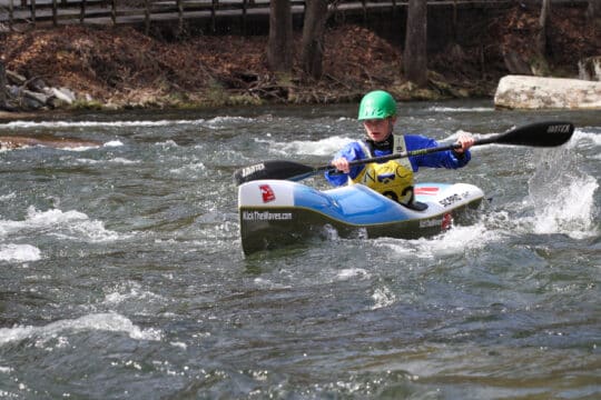 a young girl in a kayak races down in splashy water