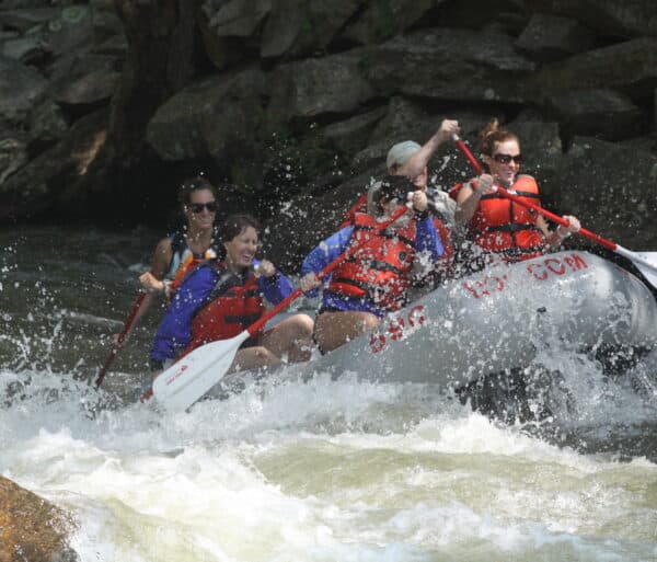 Photo of a group of paddlers hitting a white water rapid while enjoying themselves.