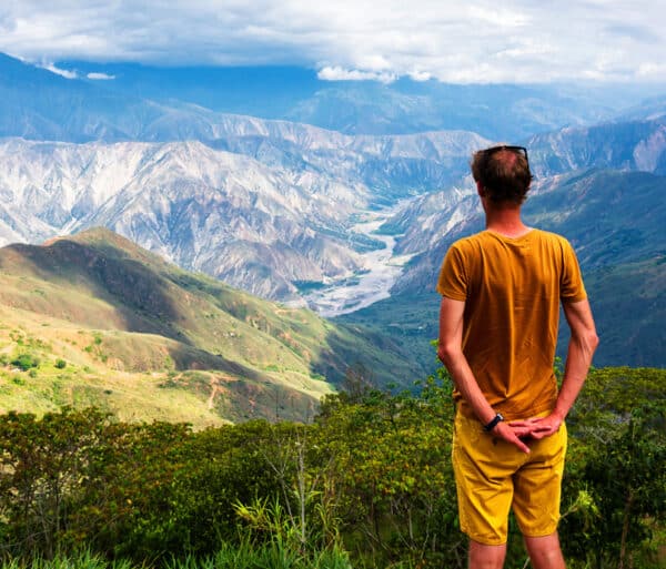 a man in an orange shirt looks over cloud covered mountain ranges at a high altitude in colombia