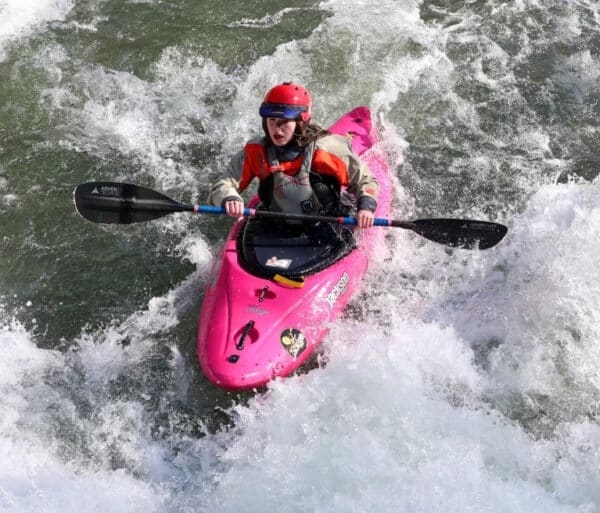a woman sits in a pink boat with paddles in splashy water