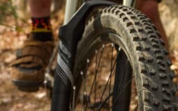 A photo showing an up close image of a mountain bike tire, with a riders foot in the distance.