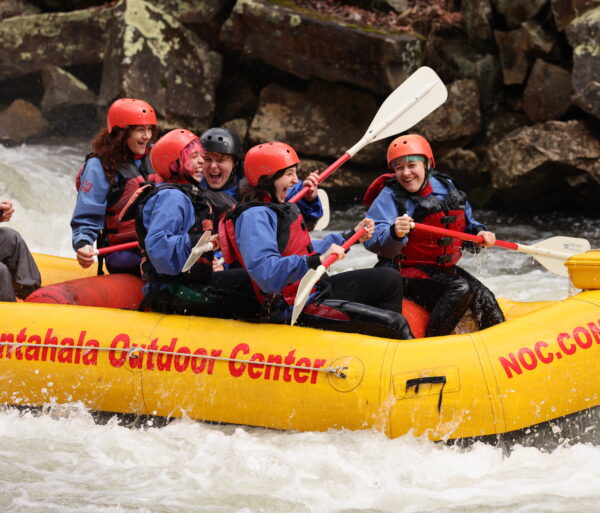 A group of rafters in helmets and PFDs take a yellow raft down the Nantahala River