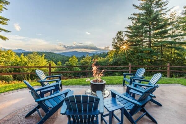 Fire pit with five Adirondack chairs overlooking greenery and mountain range.