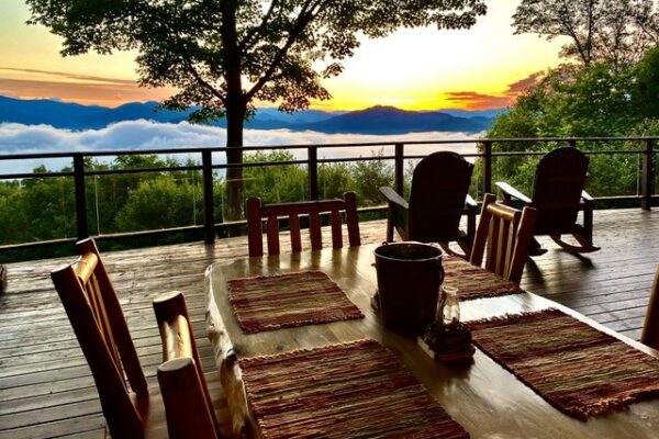 Part of a dining table on an outdoor deck with Adirondack chair facing a mountain sunset.