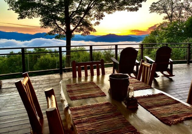 Part of a dining table on an outdoor deck with Adirondack chair facing a mountain sunset.