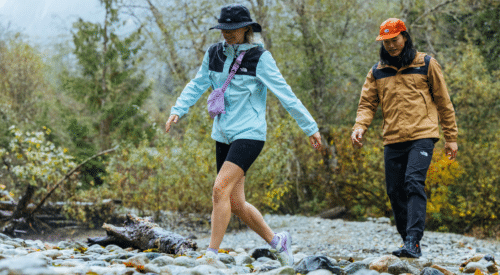 two hikers cross a rocky creek wearing north face gear.