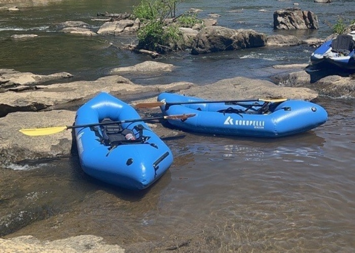 A photo of two blue packrafts waiting on the edge of a bank on a river.