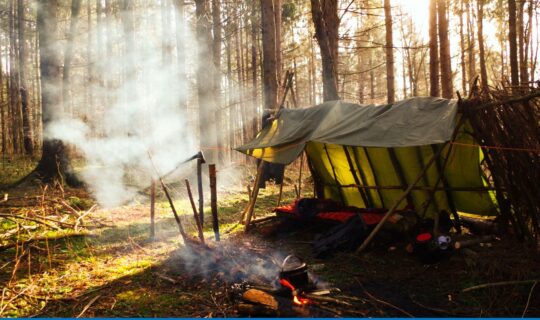 An outside shot that shows a makeshift camping area with fumes of smoke swirling from a dying fire.