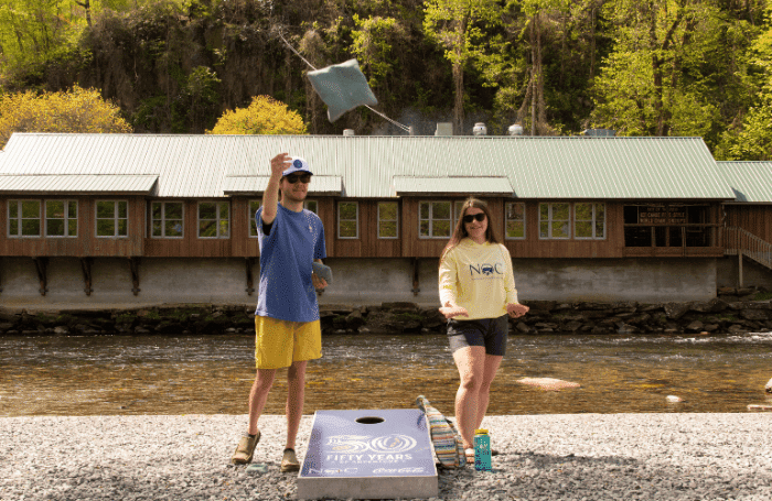 Two people playing a game of cornhole while wearing Nantahala Outdoor Center gear.