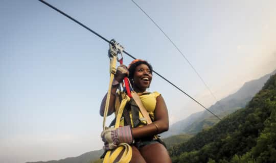 A guest ziplines in the Nantahala Gorge, surrounded by trees and blue sky.