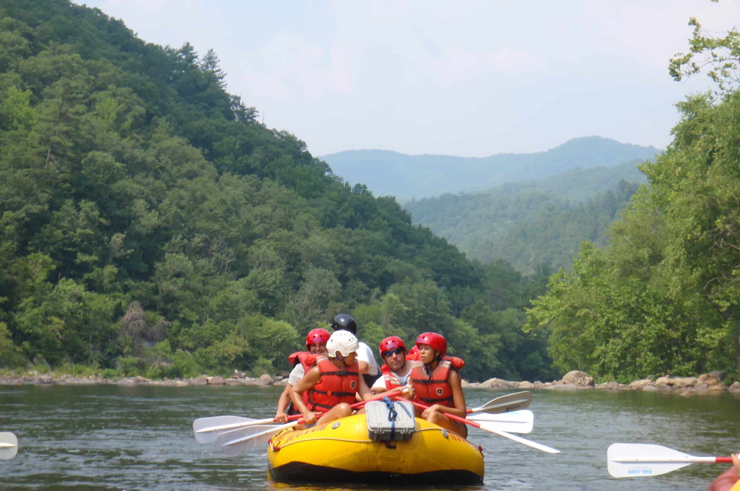 Guests in a raft on the scenic French Broad River surrounded by mountains.